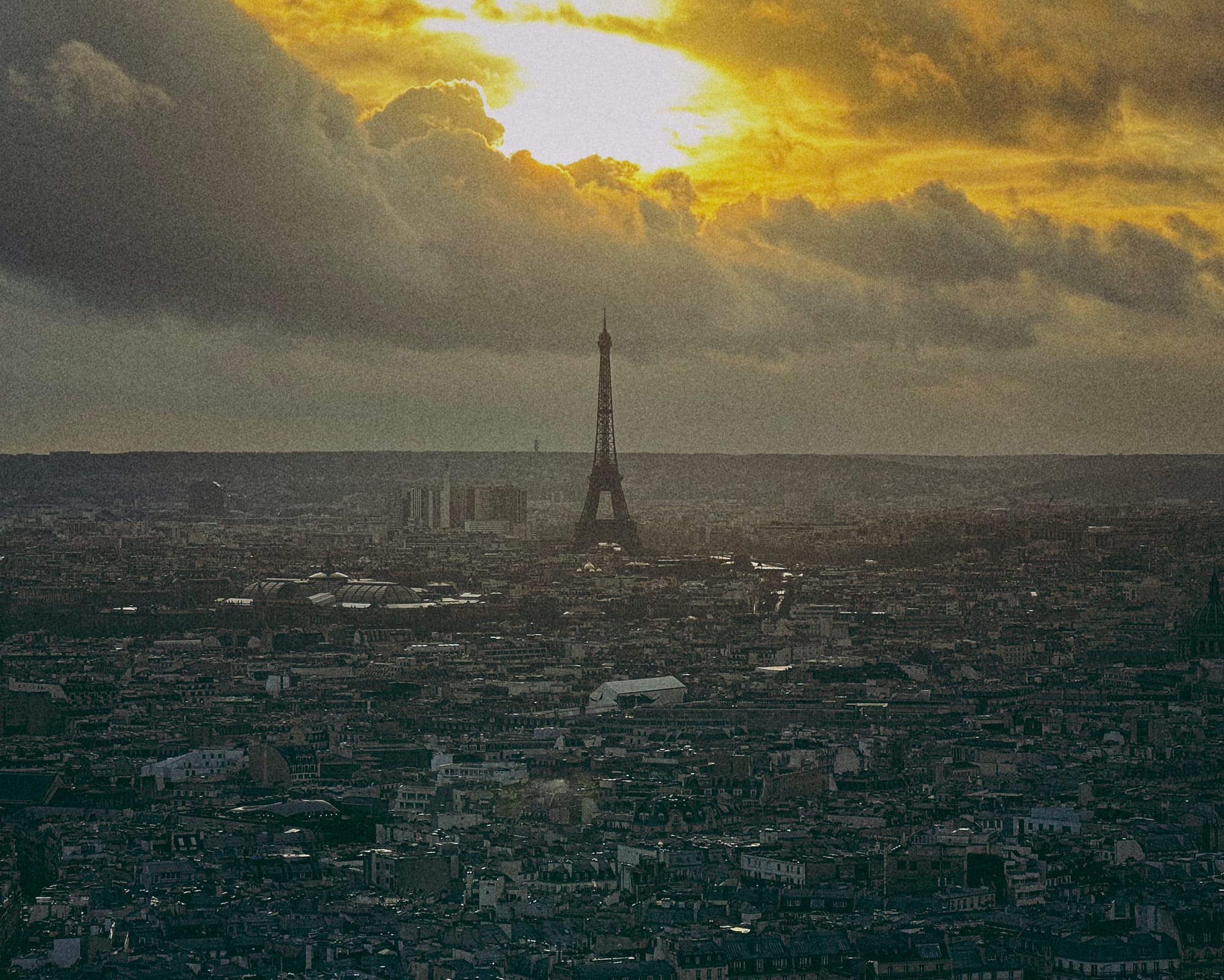 A view of the Eiffel Tower from Sacré-Cœur, the city of Paris a background against the setting sun in the clouds