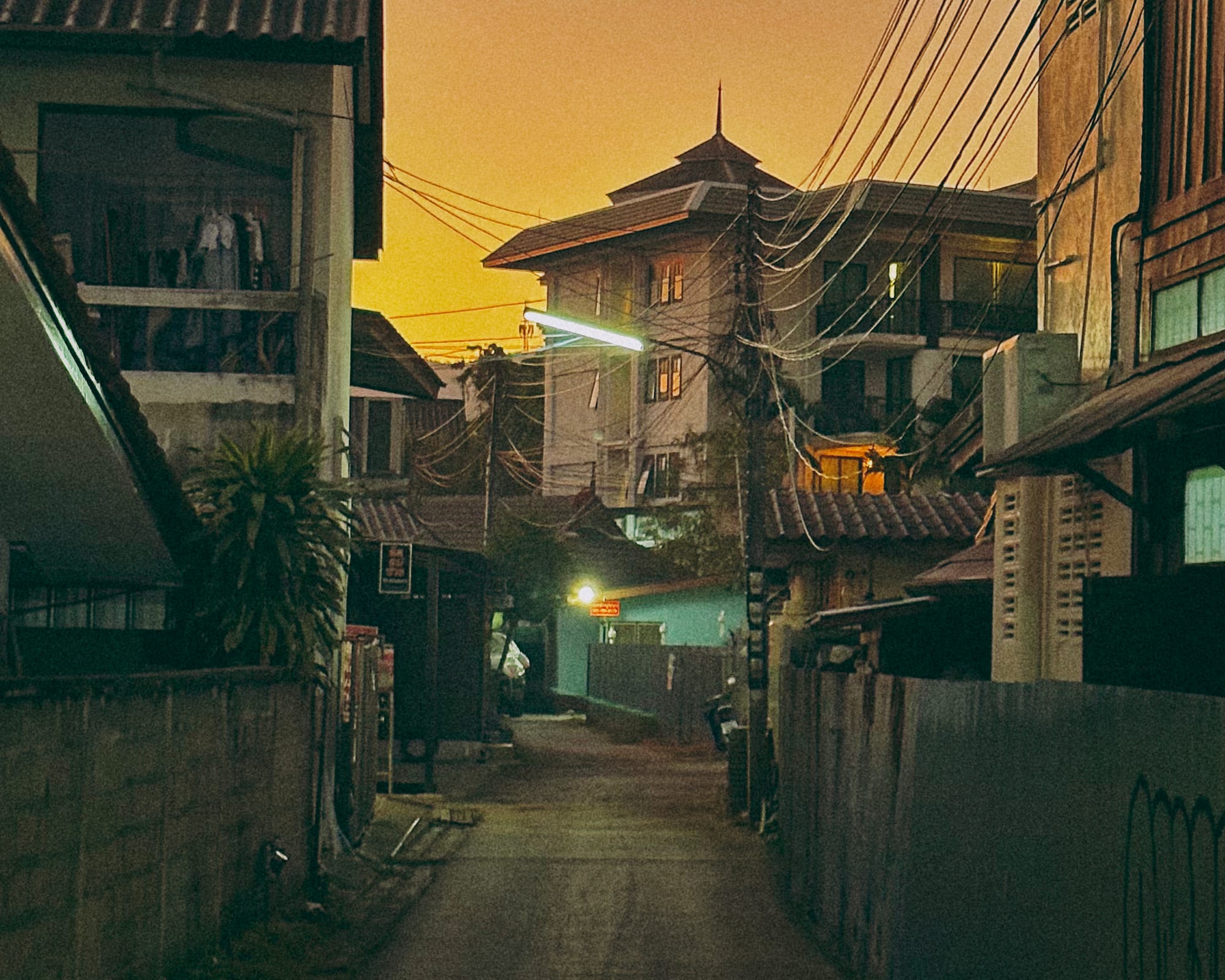A sunset in Chiang Mai. It's a small street with a flourescent lamppost. It's dusk. The sunset is amazing. 