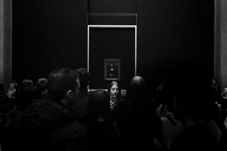 A woman in a crowd of people trying to see the Monna Lisa is turned in the opposite direction, looking at her phone.
